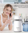 User enjoying distilled water with Heavy Duty Stainless Steel Countertop Water Stiller That Makes Up To Six Gallons Distilled Water Daily For Healthier Hydration Essential Oil Mixing And Plant Care With Durable Plastic Collection Container For Home Use.