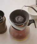 Japanese Ceramic Coffee Filter With Reusable Blue Dripper Stand And Eco Friendly Micropore Design For A Smooth Next Level Pour Over Brew That Truly Hits Different with water being poured over coffee grounds.
