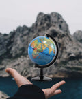 Compact Four Inch Globe For Kids And Classroom Learning Portable Desktop World Map With Latitude Scale held against mountain backdrop
