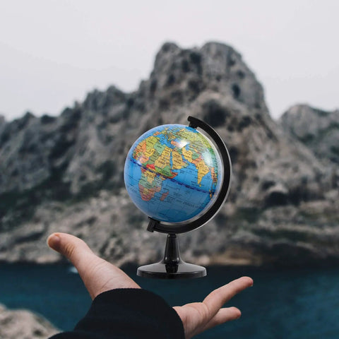 Compact Four Inch Globe For Kids And Classroom Learning Portable Desktop World Map With Latitude Scale held against mountain backdrop