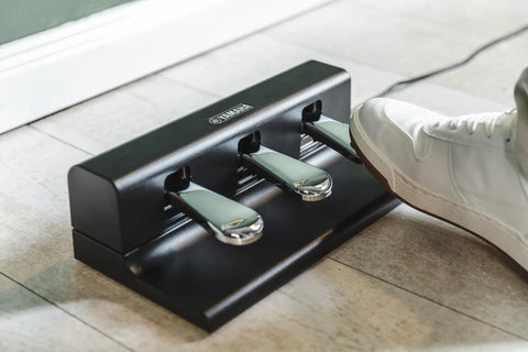 Three Pedal Foot Controller For Digital Pianos With One Cable Non Slip Rubber Base Authentic Pedal Feel For Home Studio Or On The Go FC35 Style Expressive Sustain Soft And Sostenuto Performance in use on tiled floor with sneaker stepping on pedal.