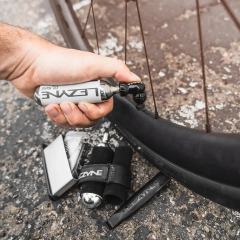 Twin Speed CO2 Inflator Bike Repair Kit with lever used on flat tire next to bike wheel with cartridges and tools