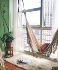 Handmade Boho Macrame Fringe Double Hammock Swing Net Chair For Two People Ultra Cozy Outdoor Indoor Patio Beach Yard Decor 95 Inches By 59 Inches Heavy Cotton Blend For Extra Comfort And Durability in a cozy room setting with sunlight streaming through windows.