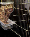 Auto Slider No Mess Bird Food Dispenser With Clear Acrylic Bowl mounted on a bird cage, filled with birdseed for parakeets.