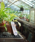 Analog Hygrometer Thermometer For Indoor Outdoor Use No Battery Required Easy To Read Humidity And Temperature Gauge With Celsius Fahrenheit For Patio Garden Cellar Greenhouse Closet in a greenhouse with potted plants.