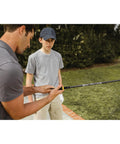 Man demonstrating Golf Grip Trainer Club Attachment to a boy for correct hand positioning on a golf club outdoors.