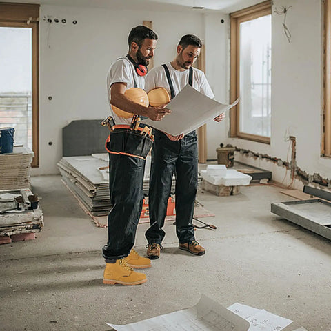 Two men in a construction site wearing Rugged Leather Steel Toe Work Boots For Men, Oil And Slip Resistant, Size US 10.5W, holding plans.
