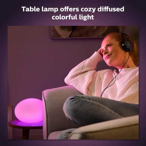 Person relaxing with Flourish Smart Table Lamp White With Color Ambiance LED Color Changing Bulb on side table, emitting pink diffused light