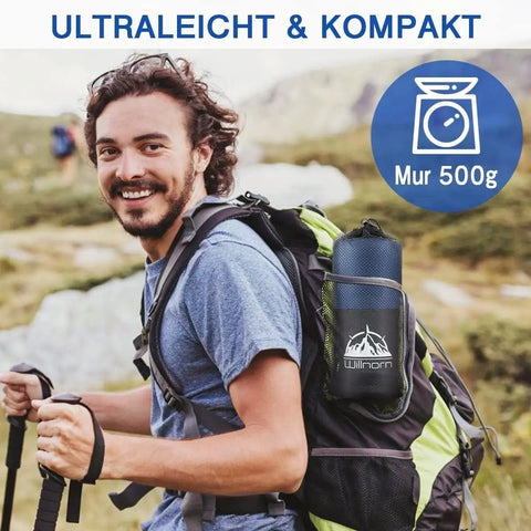 Hiker carrying a backpack with a compact sleeping bag liner, ideal for camping trips under 500g, in mountain scenery.