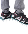 Lawn Aerator Sandals Spiked Shoes for Yard Work with iron spikes and 3 straps, worn over sneakers on a patio surface.