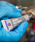 Permatex Nickel Anti-Seize lubricant tube held in blue-gloved hand (close-up), 8 oz.
