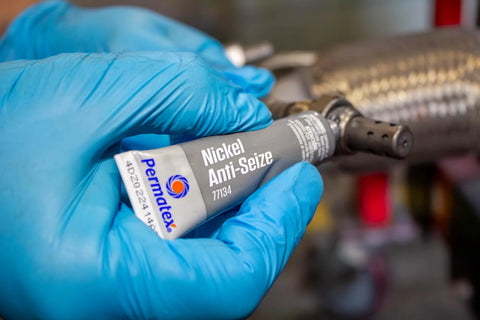 Permatex Nickel Anti-Seize lubricant tube held in blue-gloved hand (close-up), 8 oz.