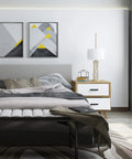 Modern bedroom interior with geometric art, white nightstand, and a neatly made bed with gray accents.
