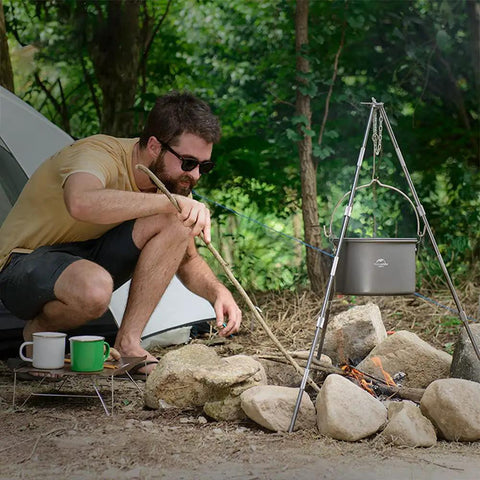 Man cooking with Ultralight Aluminum Hanging Camping Pot With Lid, 4.2 Quart Cookware For 4 To 6 People over campfire
