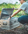Rugged Folding Storage Box With Lid Heavy Duty Aluminum Frame Stackable Gear Crate Built Tough For Camping And Picnics, hands opening lid.