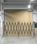 Straight Up Heavy Duty Expandable Metal Barrier On Wheels, Adjustable Retractable Safety Fence For Crowd Control, Rolling Traffic Gate With Locking Casters, Foldable Industrial Yard Barrier, Coffee Brown, shown in a warehouse.