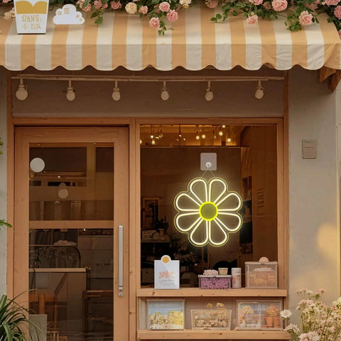 Flower Neon Sign Daisy Window Light LED Warm White For Bedroom Decor hanging in a cozy shop window display.