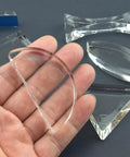 Hand holding semicircular lens from Six Piece Acrylic Glass Light Prism Set For Physics Lab Teaching, surrounded by other prisms and lenses.
