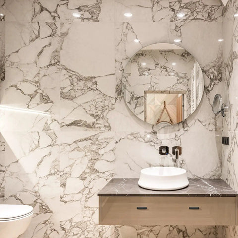 Modern bathroom with marble walls, round mirror, and sleek sink