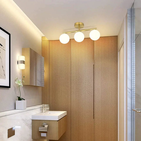 Three Light Vanity Light Fixtures In Gold Brass Finish With Dimmable Wall Sconce For Bath Mirror Milk Glass Shades With G9 Base Mid Century Modern Style Sleek Retro Vibe over wood finish bathroom cabinetry.