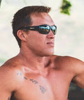Man wearing Floating Safety Sunglasses With Matte Black Frame And Smoke Lenses, Non Slip Gray Foam Padding, ANSI Z87 Plus Certified outdoors.