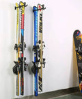 Skis and snowboard hanging on wall-mounted heavy duty garage hooks for tool organization and storage.