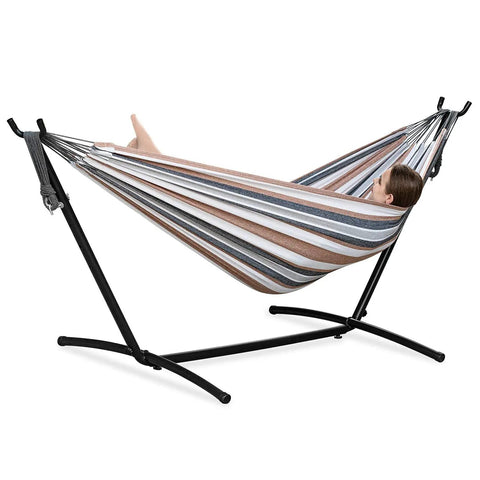 Double Hammock With Stand For Outdoor And Indoor Use Portable Space Saving Heavy Duty Steel Frame Easy Assembly 2 Person Capacity 450 Lbs Kick Back Coffee featuring a striped fabric and black stand with a person relaxing.