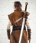 Back view of medieval costume with Back Sword Holster Leather Sword Holder With Adjustable Buckle on white brick background.