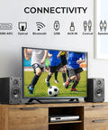 Powered Bookshelf Speakers With Wireless 100W RMS Bluetooth And EARC beside TV displaying soccer in home setup