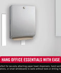 Heavy Duty Mounting Tape 12 Foot Roll Holds Up To 10 Lbs secures a paper towel dispenser on a wall in an office setting.