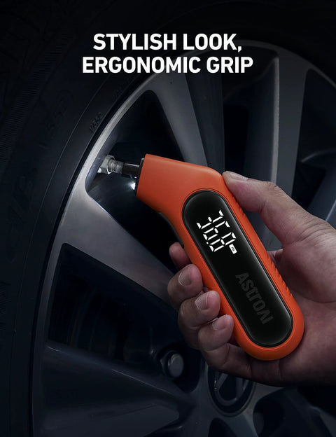 Orange AstroAI digital tire pressure gauge with backlit display held at a car tire valve showing PSI