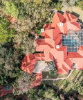 Aerial view of a red tile roofed house surrounded by trees, depicting the Heavy Duty Tile Roof Glaze And Clear Shielding Sealant With Urethane Reinforced Strength For Tough As Nails Weather Barrier And A Sleek Satin Finish That Gonna Save Your Tiles From Failing In A Practical Five Gallon Size.