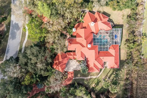 Aerial view of a red tile roofed house surrounded by trees, depicting the Heavy Duty Tile Roof Glaze And Clear Shielding Sealant With Urethane Reinforced Strength For Tough As Nails Weather Barrier And A Sleek Satin Finish That Gonna Save Your Tiles From Failing In A Practical Five Gallon Size.