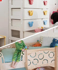 White drawer with colorful Mickey-shaped knobs, child playing on wooden bed with playful design, cozy bedroom setup.