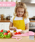 Toy kids knife set with cutting board and pink utensils; girl in yellow apron slices vegetables.