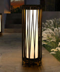 Outdoor Solar Floor Lamp With Rattan Trim And Steel Frame, illuminating a patio with a warm glow, beside grass and steps.