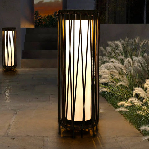 Outdoor Solar Floor Lamp With Rattan Trim And Steel Frame, illuminating a patio with a warm glow, beside grass and steps.