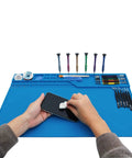 Person using Pro Grade Heat Insulation Silicone Repair Mat With Built In Scale Ruler Magnetic Parts Pockets And Screw Position Guides For Soldering Iron Phone And Computer Repair On A 22 By 14 Inch Workbench Pad for phone repair, tools visible.