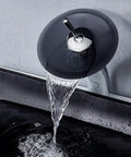 Smooth swivel faucet pouring water into a sleek black rectangular vessel sink made from heavy duty tempered glass.