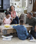 Family playing board game on carpeted living room floor, near beige sofa, emphasizing cozy home atmosphere.