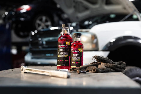 Shift Restore Transmission Additive 32 Oz bottles on garage workbench, focus on product label in car repair setting