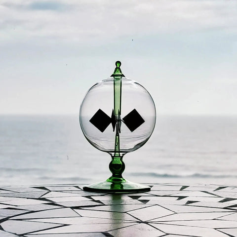 Green Solar Power Radiometer Glass Windmill Desk Decor That Spins With Light Crookes Radiometer on modern surface with ocean view.
