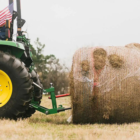 Dual Design Gooseneck Tractor Trailer Hitch With Hay Bale Spear Charcoal Frame Two Inch Receiver Mount And Two Five Sixteenth Inch Gooseneck Ball in use lifting a large hay bale
