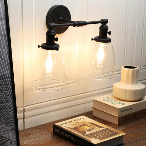 Retro Industrial 2-Light Wall Sconce Set with dual bell-shaped clear glass lampshades, black finish, illuminating a desk area.