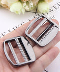Hand holding two heavy duty gunmetal zinc alloy ladder lock sliders for adjustable webbing straps