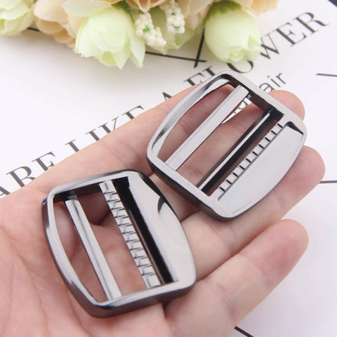 Hand holding two heavy duty gunmetal zinc alloy ladder lock sliders for adjustable webbing straps