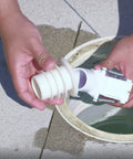 Person holding adjustable Flowkeeper valve regulator for automatic pool cleaners above inground pool system opening.