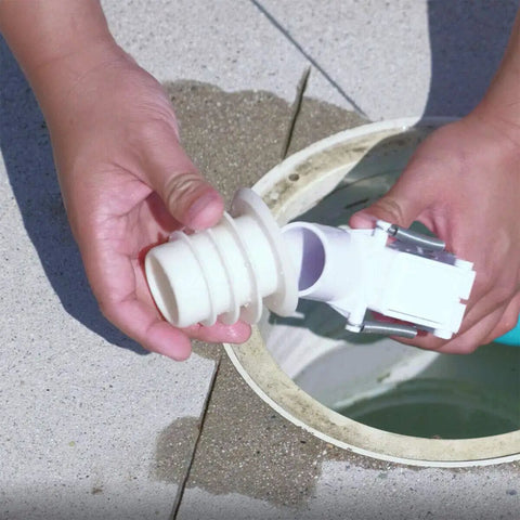 Person holding adjustable Flowkeeper valve regulator for automatic pool cleaners above inground pool system opening.