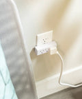 Premium Grounded Outlet Extenders Four Pack Triple Socket Wall Power Splitter plugged into wall beside a potted plant.