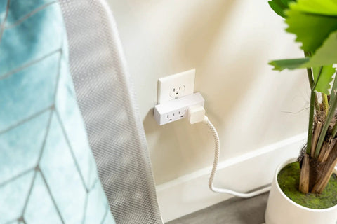 Premium Grounded Outlet Extenders Four Pack Triple Socket Wall Power Splitter plugged into wall beside a potted plant.